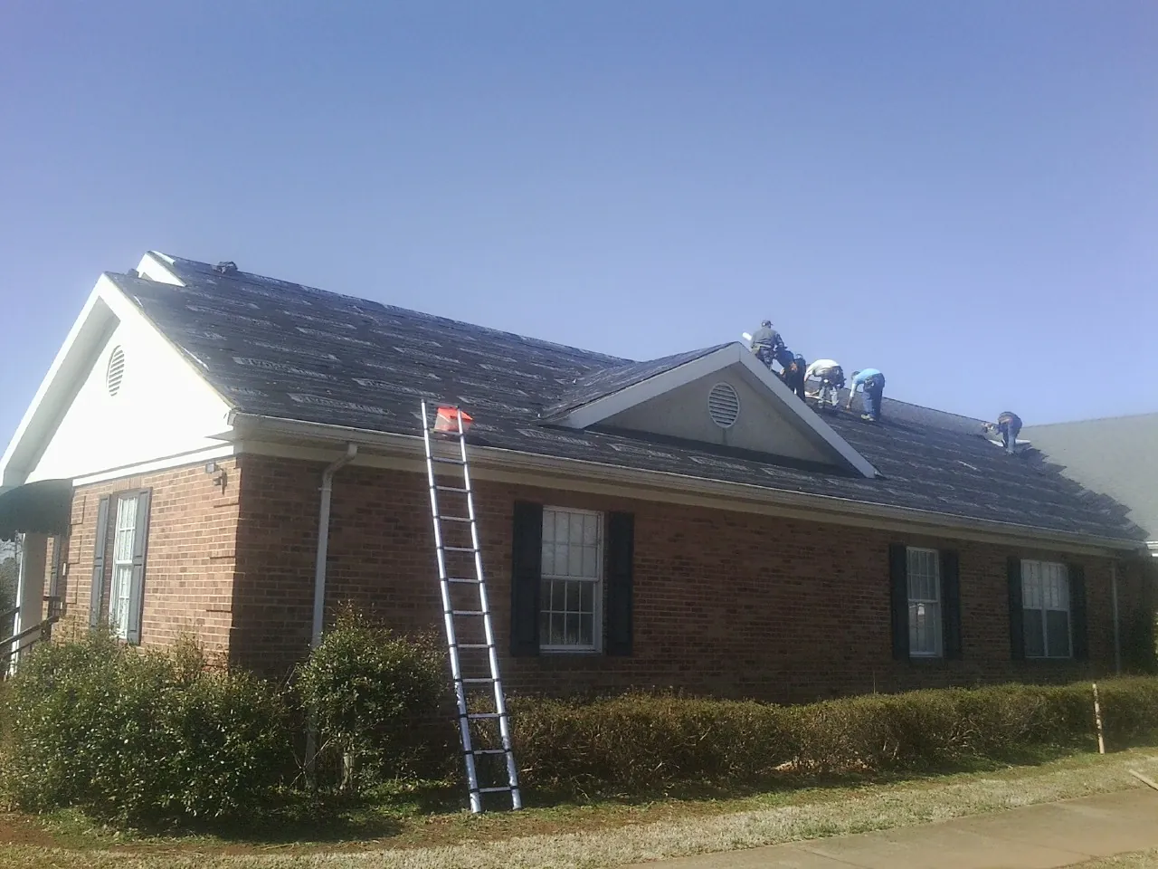 Crew tearing shingles off a brick ranch roof with a ladder set — Metal Roof Repair work by our crew in Rogue River