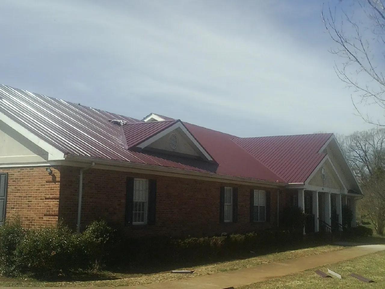 Red metal roof with gabled entries on a long brick building, from a Hail Damage Roof Repair job in Rogue River
