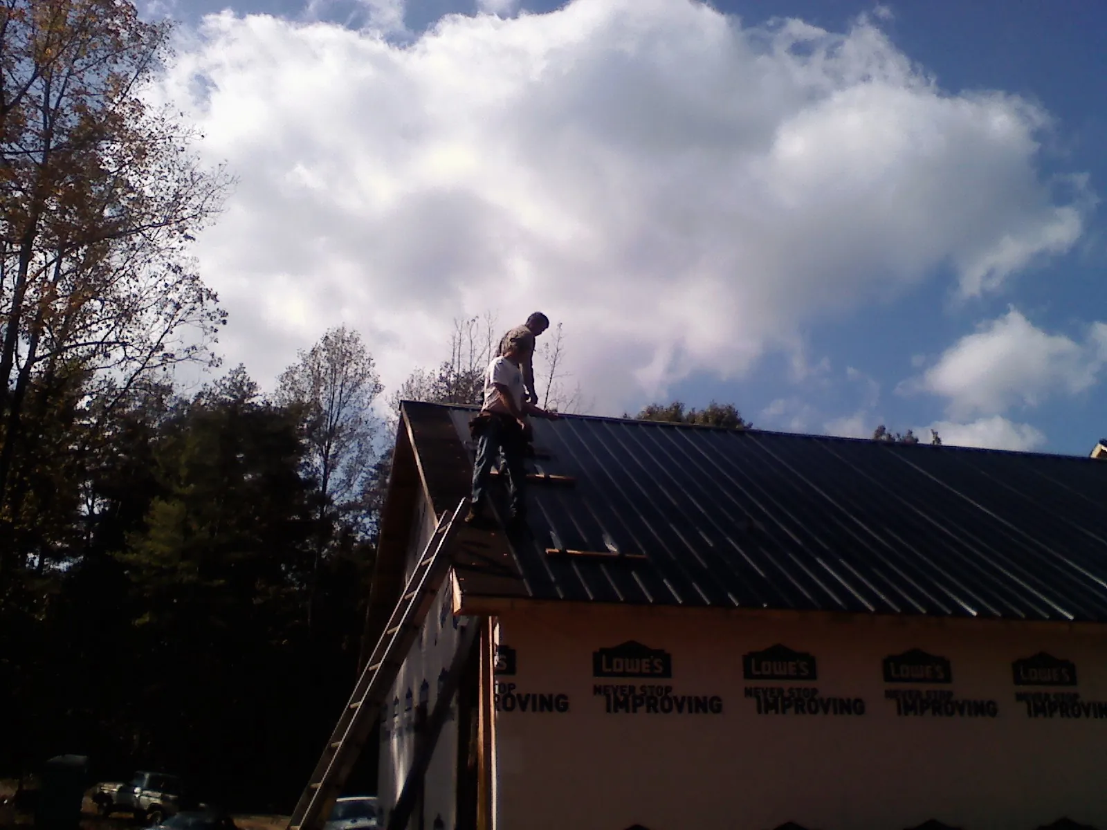 Roofer fastening dark metal panels high against a cloudy sky, from a Roof Inspection job in Rogue River