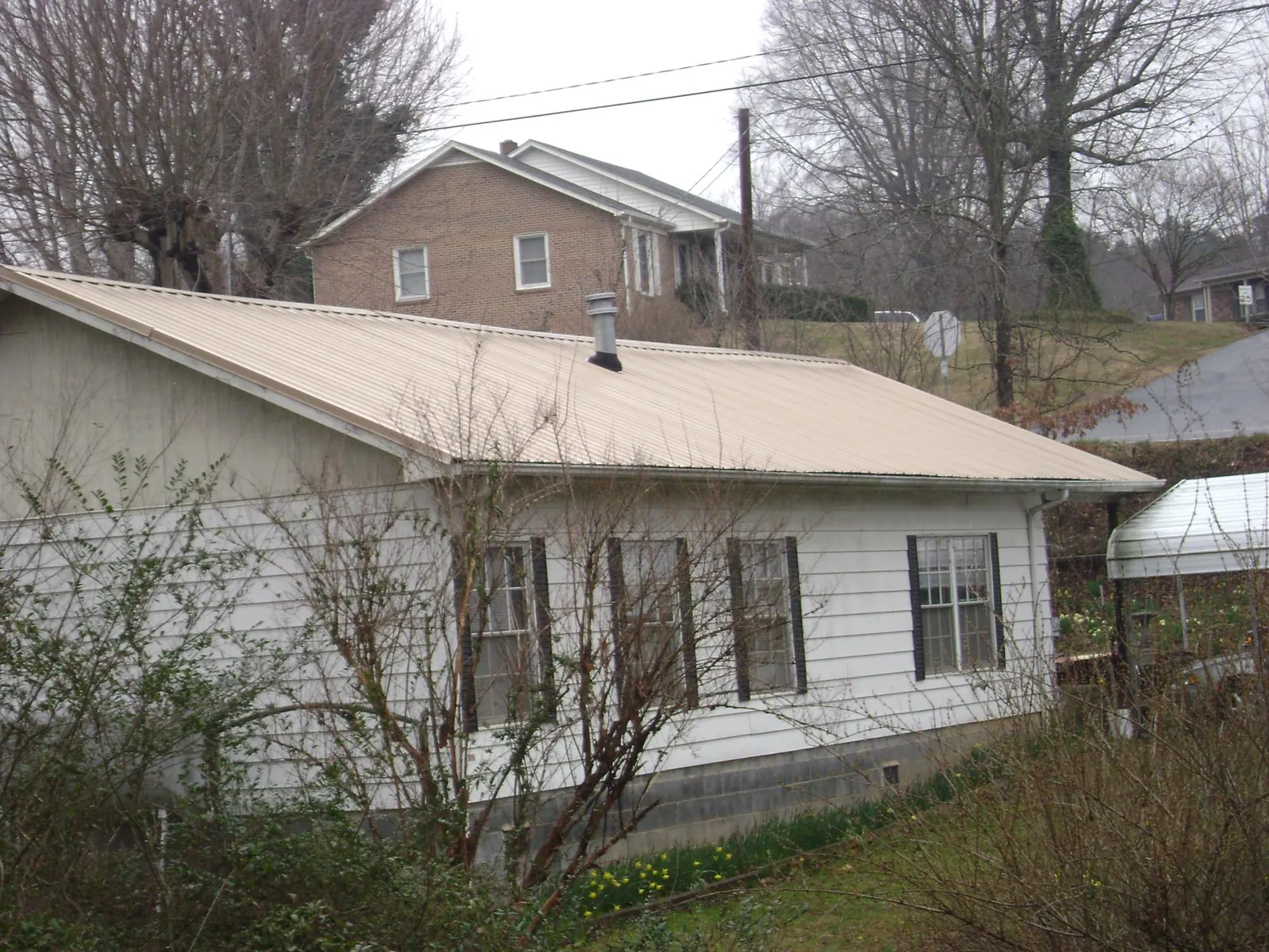 Tan metal roof on a white sided house set into a hillside — Commercial Roofing by Roofing Brothers in Rogue River